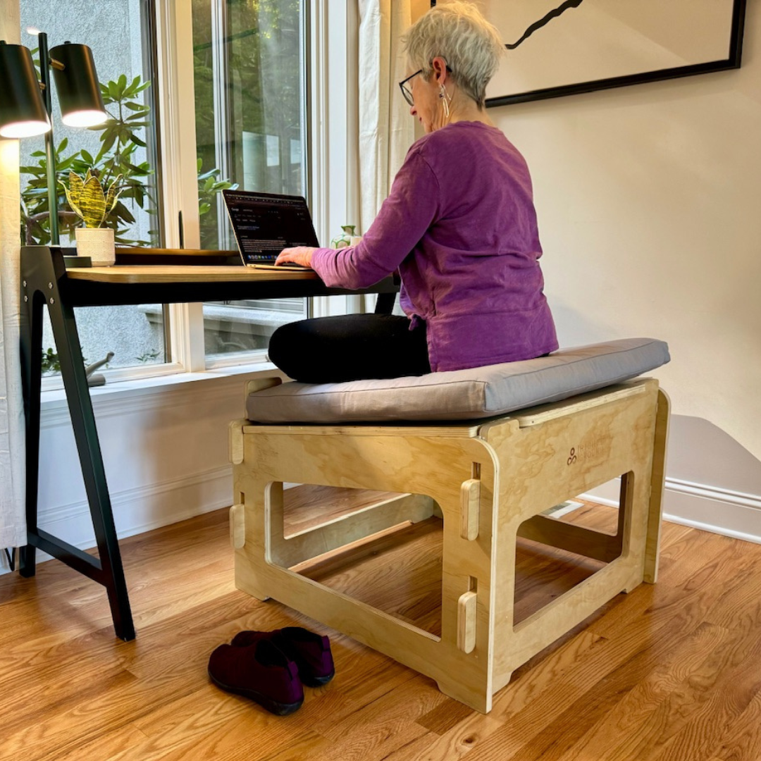 Mature woman using a laptop and sitting cross-legged at a desk on a Higher Ground Chair