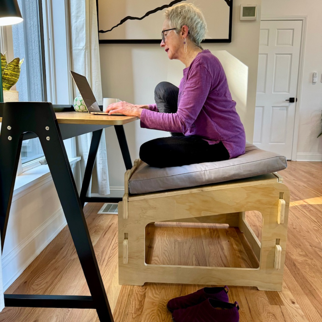 Mature woman sitting with one knee up on a higher ground chair and grey cushion