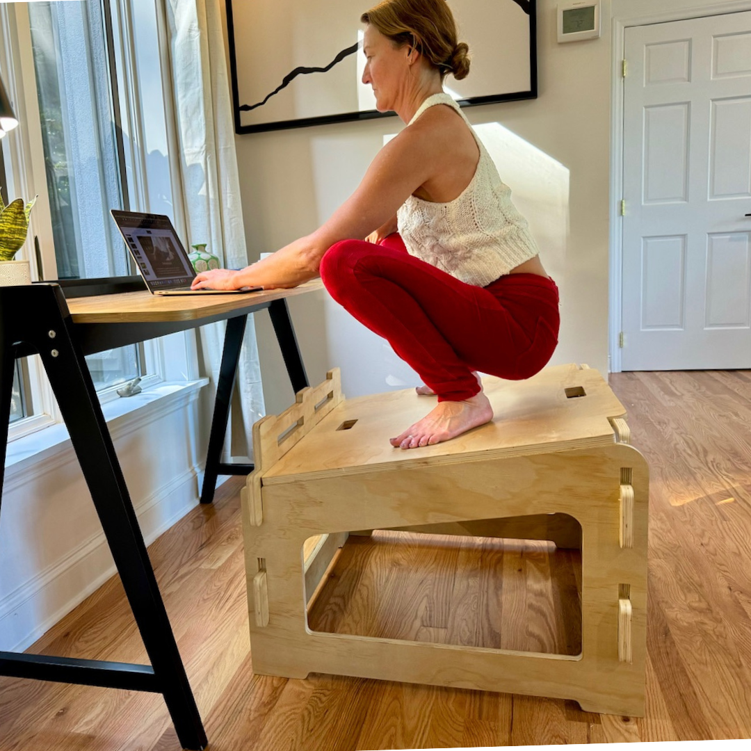 Woman squatting on higher ground chair and working on laptop