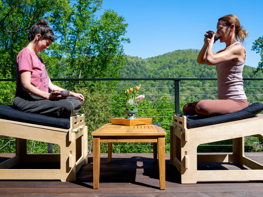 Two women sitting cross-legged on a deck drinking Japanese tea