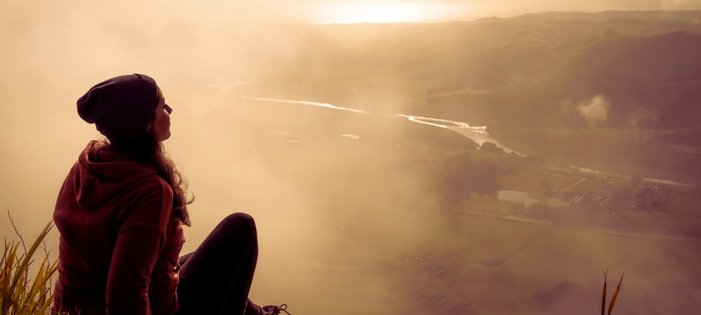 A woman sitting on a hill looking at a foggy landscape