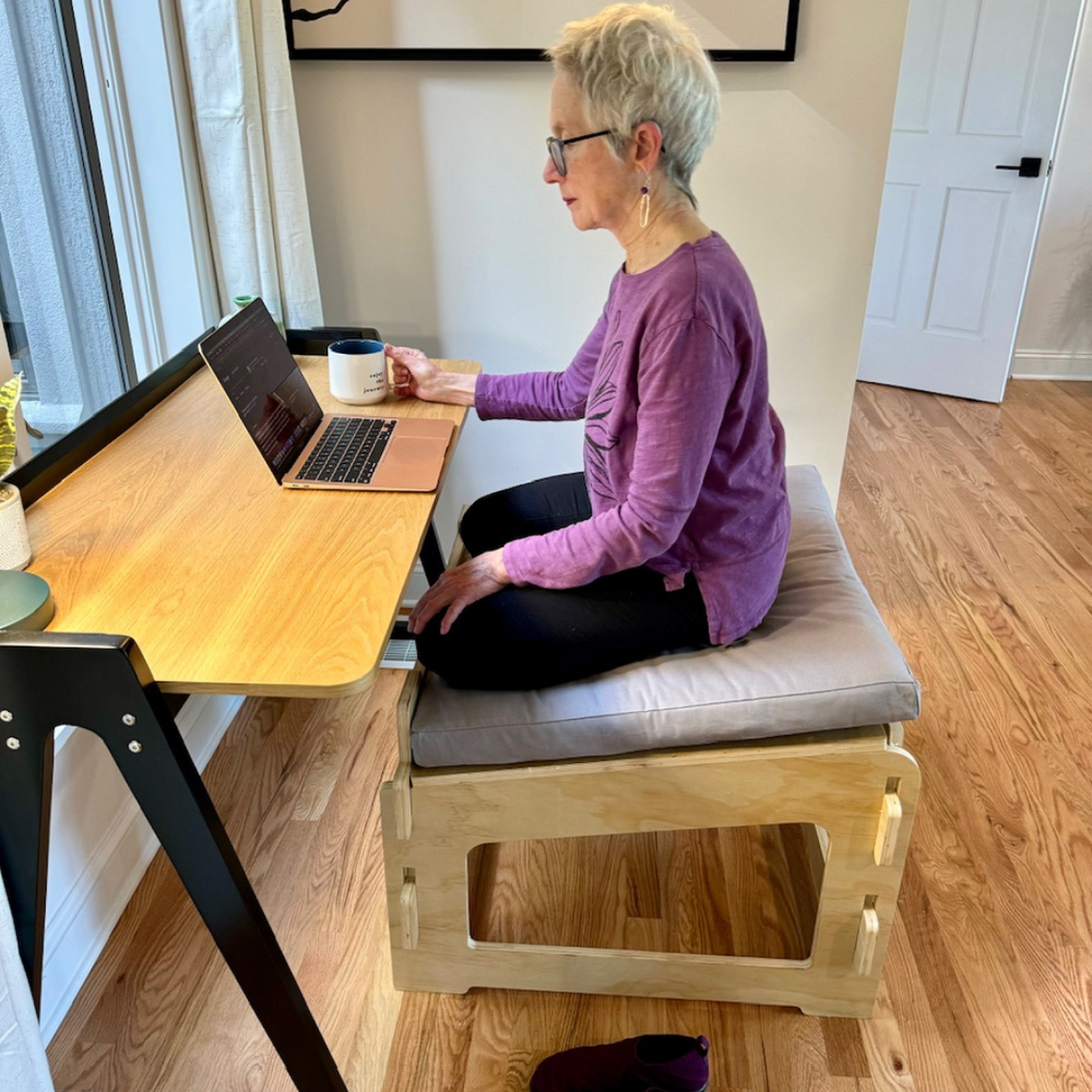 
                      
                        Mature woman using a laptop and sitting cross-legged at a desk on a Higher Ground Chair
                      
                    