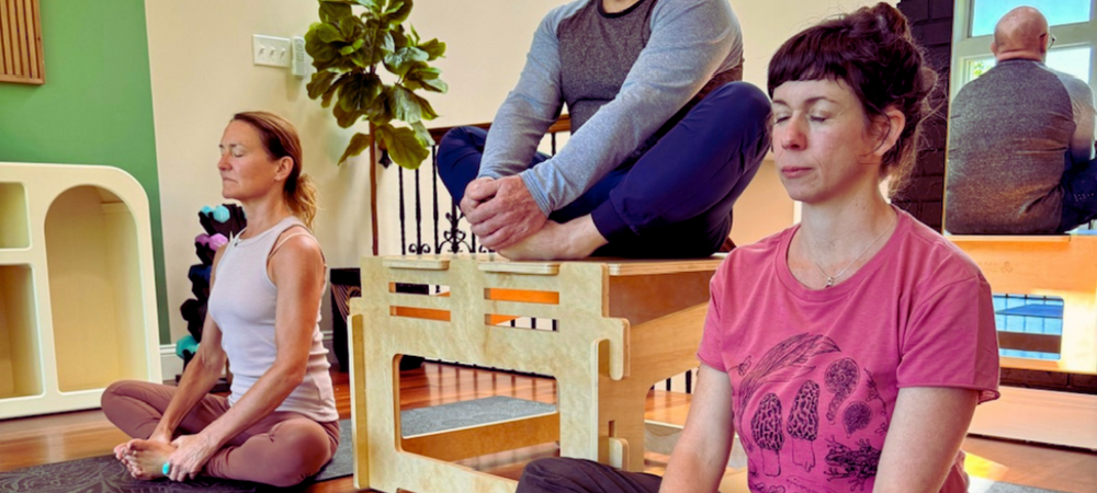 Two woman meditating on the floor and a man meditating on a chair