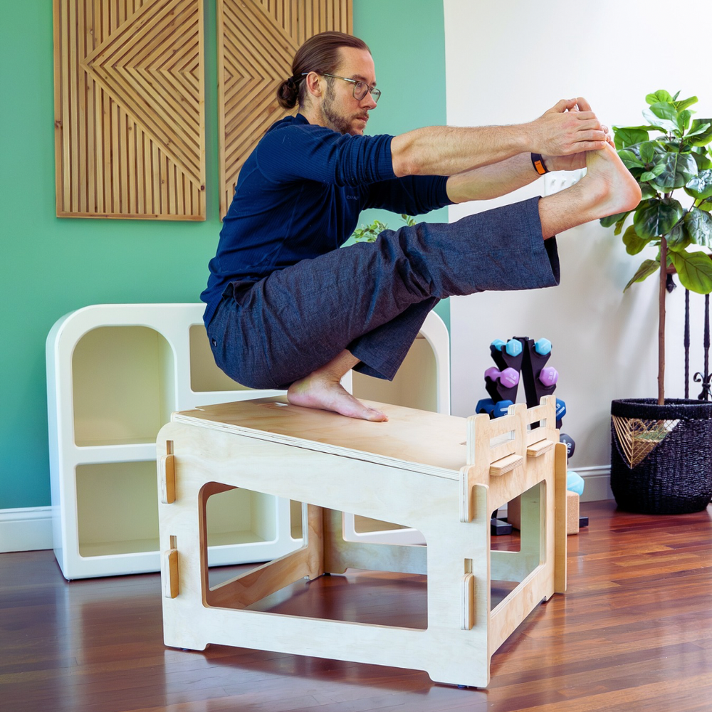 A man holds one foot with both hands while doing a pistol squat on a chair